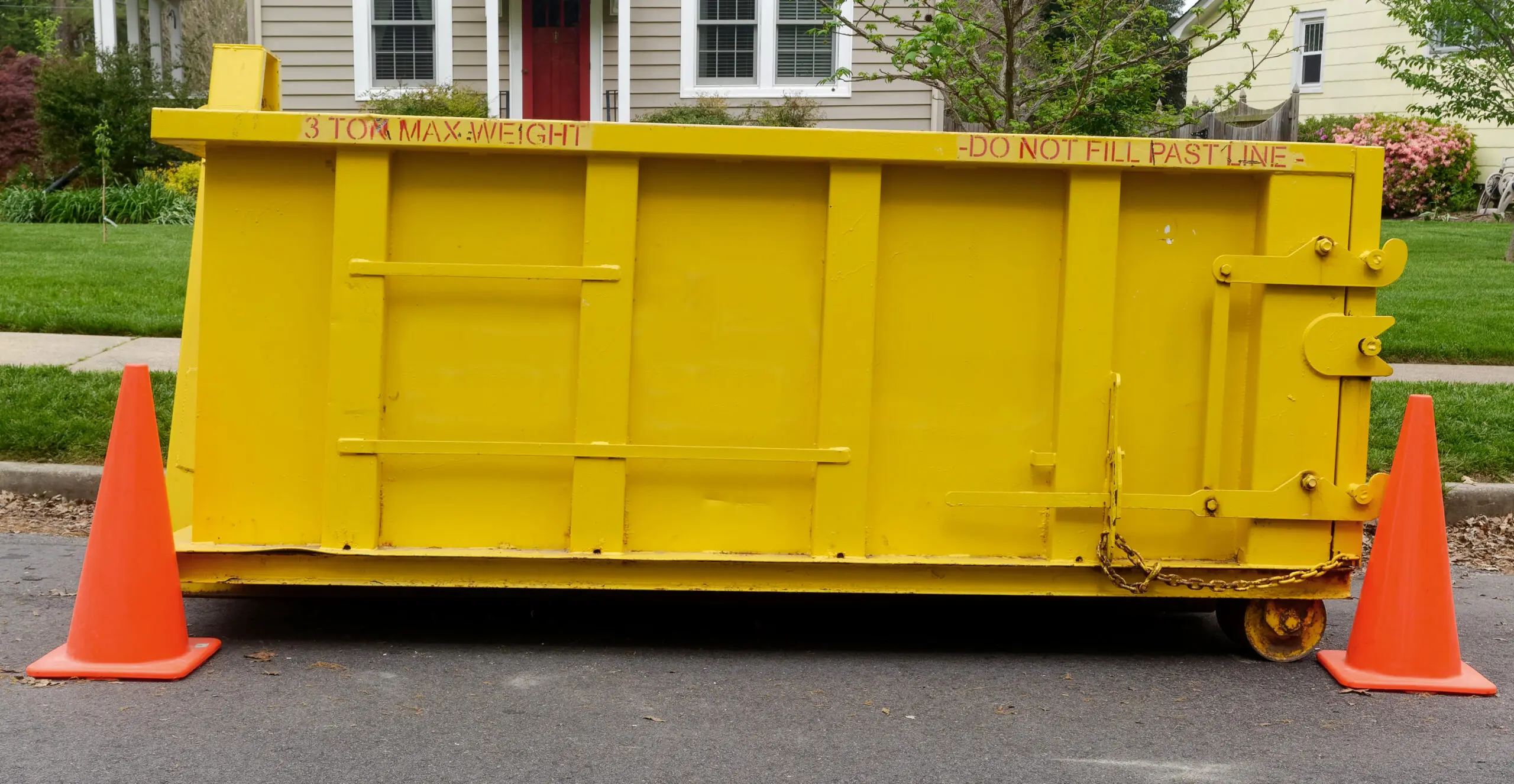 Yellow construction dumpster standing in front of neighborhood home.